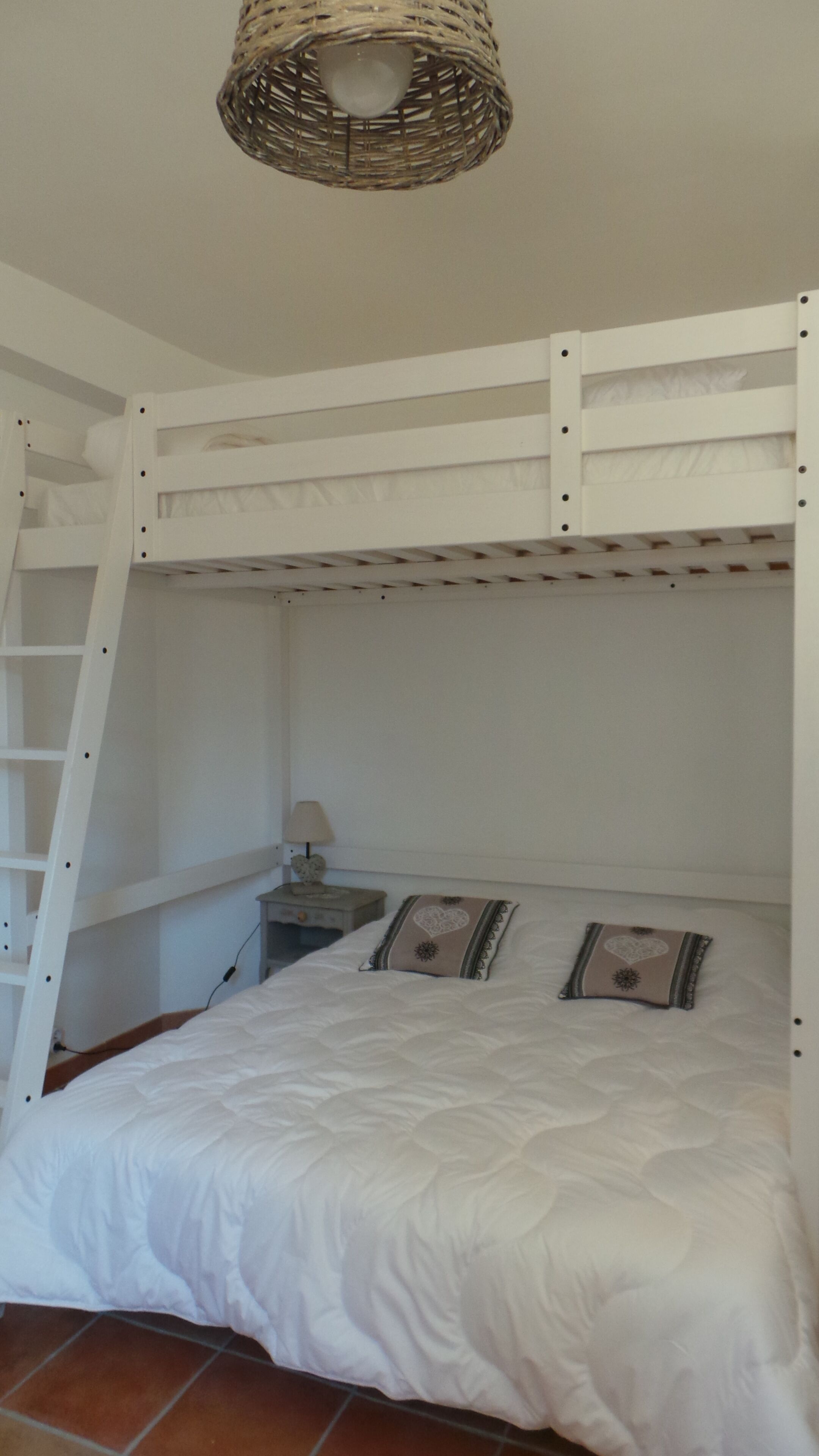 A bunk bed room with a ladder, a bedside table, and a lamp.