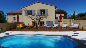 Una casa de dos pisos con piscina, mobiliario de exterior y un árbol.