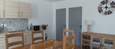 A compact kitchen with wooden cabinets, a dining table with chairs, a clock, and a cabinet with drawers.