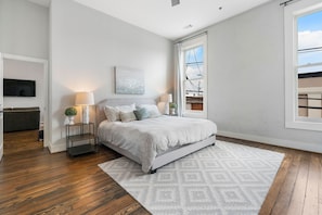 A bedroom with a bed, two bedside tables, a TV, and a window with a view of a balcony.