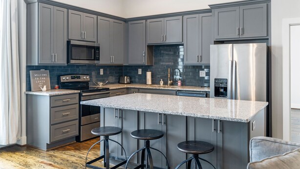 A modern kitchen with grey cabinets, stainless steel appliances, a granite countertop, and three stools. - Downtown Cartersville 1BR Loft 1 (Cartersville)
