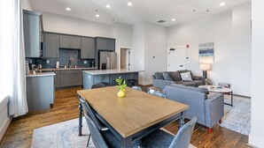 A modern kitchen with grey cabinets, a wooden dining table, and a living area with a grey sofa and a coffee table. - Downtown Cartersville 1BR Loft 1 (Cartersville)