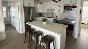 Una cocina moderna con armarios blancos, electrodomésticos de acero inoxidable y una isla central con taburetes.