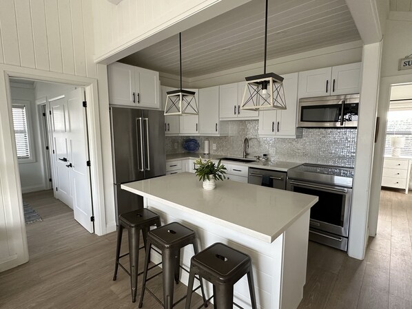 A modern kitchen with white cabinetry, stainless steel appliances, and a central island with stools.