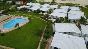 Un complejo turístico con varias cabañas de techo blanco, piscina y vista a la playa.