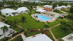 Zona residencial con piscina rodeada de casas blancas, palmeras y vistas al agua.