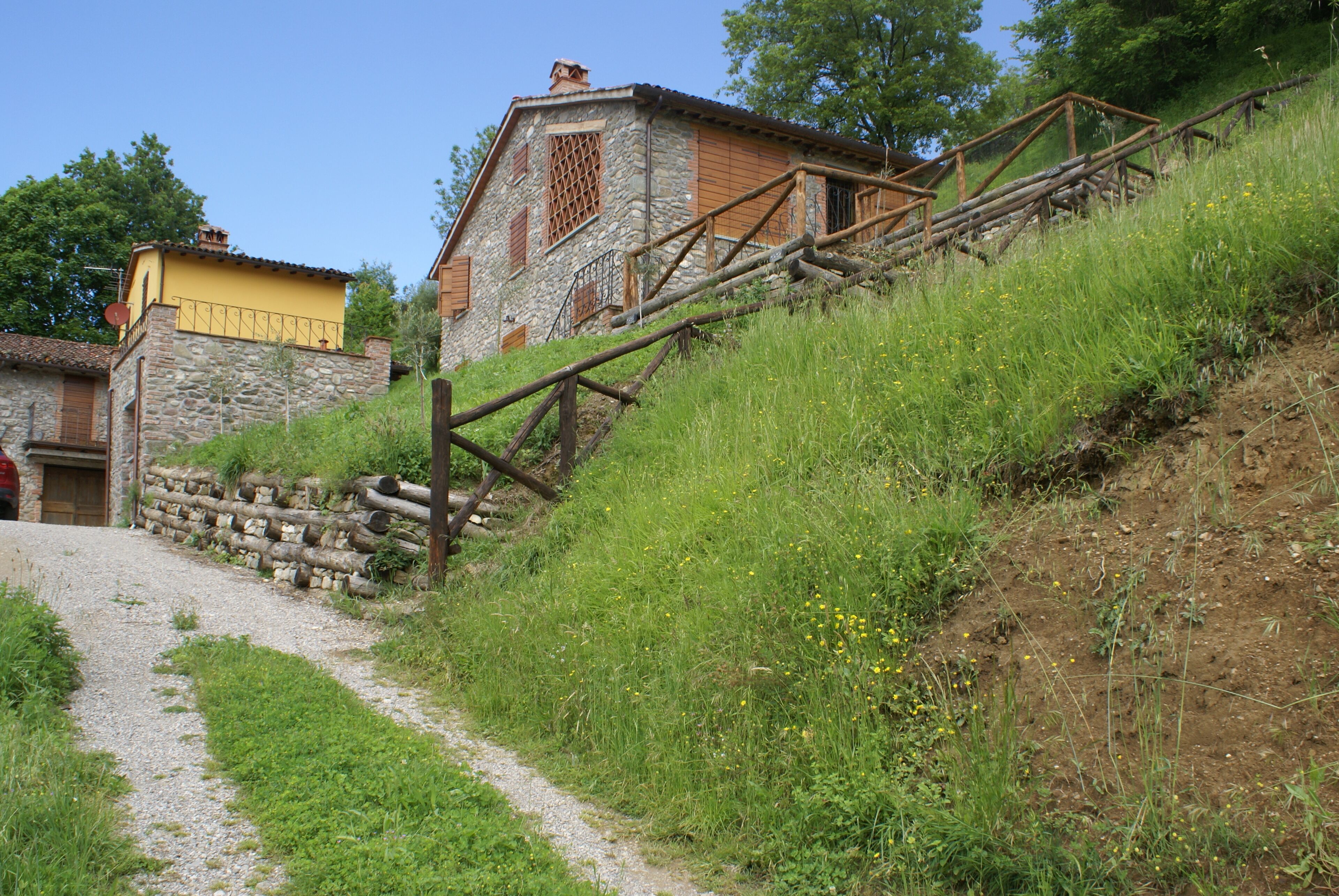 Un bâtiment rustique en pierre, avec un escalier en bois menant au sommet d’une colline verdoyante.
