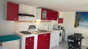 Une cuisine de taille réduite avec des meubles de rangement rouges et blancs, une cuisinière à gaz, un four à micro-ondes et un évier.