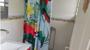Une salle de bain avec un lavabo blanc, un meuble rouge, des toilettes et un rideau de douche à motifs tropicaux.