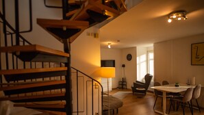 Un intérieur moderne avec un escalier en bois, un coin repas comprenant une table et des chaises, et un espace salon confortable avec une lampe.