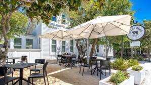 Eine Außenpatio-Terrasse mit Tischen, Stühlen, Sonnenschirmen und Pflanzkübeln.