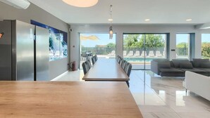 Eine moderne Küche mit einer langen Holzausziehtheke, einem integrierten Kühlschrank und einem großen Fenster mit Blick auf einen Poolbereich.