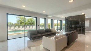 Ein großzügiger Wohnbereich mit großem Fenster mit Blick auf einen Pool, einer modernen Sofagarnitur und einem flachbildschirmfernseher, der an einer Glaswand angebracht ist.