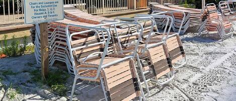 Des fauteuils de jardin sont empilés sur une zone sablonneuse, et une pancarte indique qu’ils sont réservés à l’usage exclusif de certains résidents.