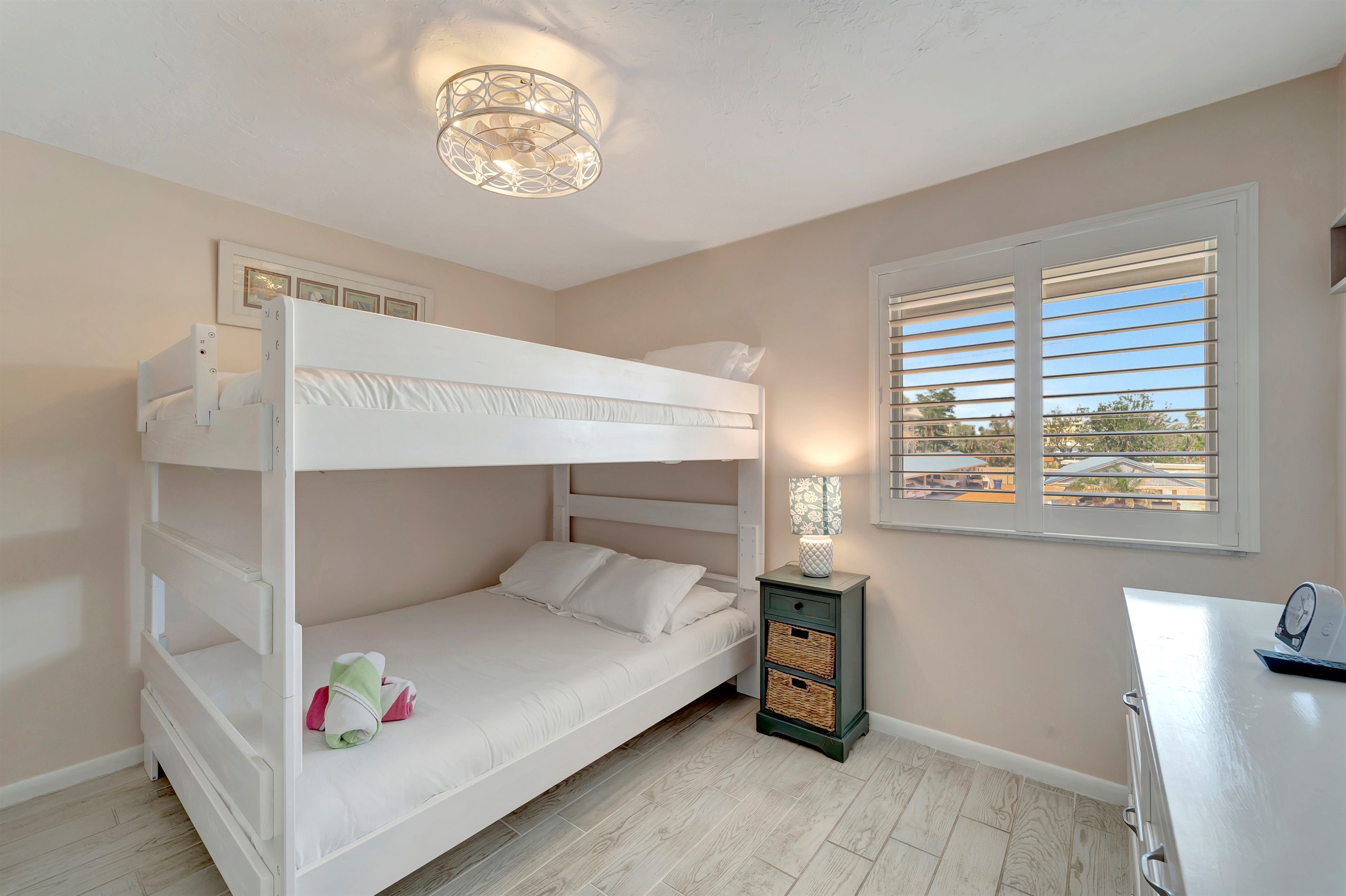 A bunk bed room with a bedside table, a lamp, and a window with blinds.