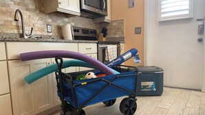 A kitchen with a blue cart, a microwave, cabinets, and a trash bin. - Spacious ~ Private Beach~Shuffleboard~Pool (Siesta Key)