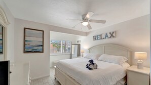 A bedroom with a bed, a ceiling fan, a bedside table with a lamp, and a wall-mounted sign that reads "RELAX". - Spacious ~ Private Beach~Shuffleboard~Pool (Siesta Key)