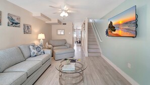 A living room with a sofa, a coffee table, and a painting of a sunset. - Spacious ~ Private Beach~Shuffleboard~Pool (Siesta Key)