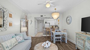 A living room with a sofa, round wooden coffee table, and a dining area with a table and chairs. - Palm Beach C22  1 bd 1.5 bth coastal inspired condo great view updated remodeled (Orange Beach)