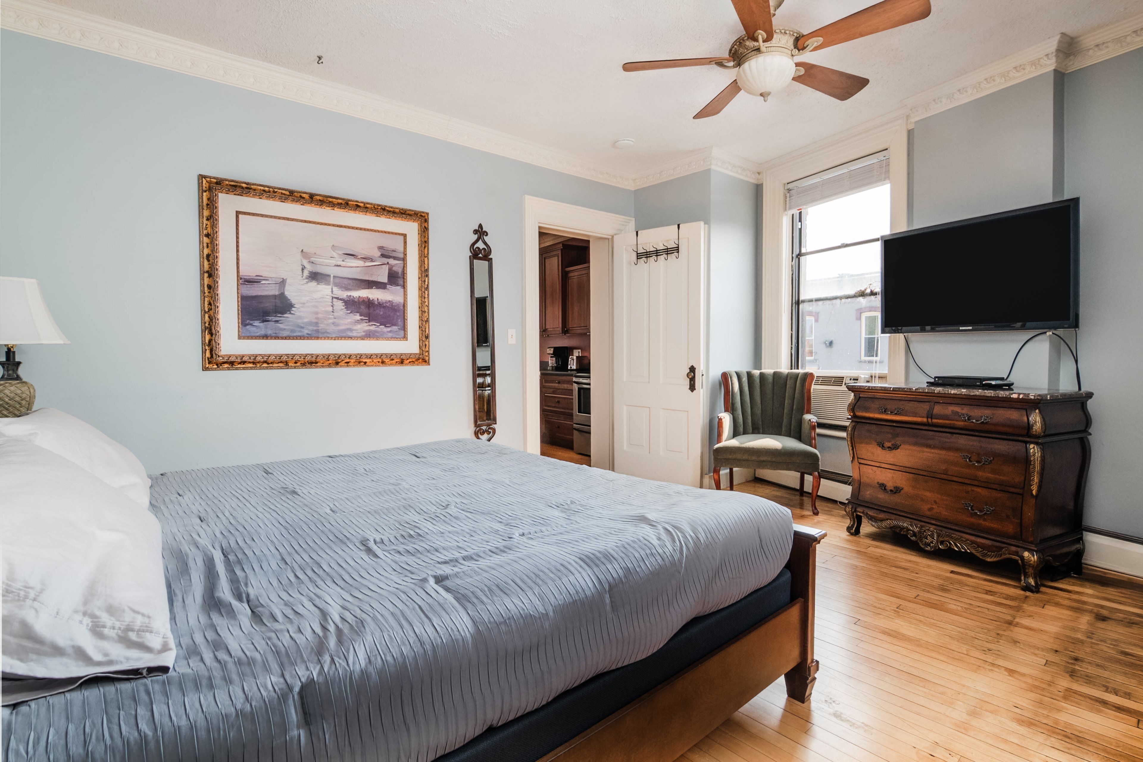 A bedroom with a bed, a ceiling fan, a dresser, a television, and a framed picture on the wall.