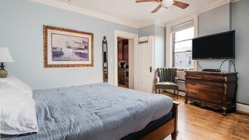 A bedroom with a bed, a ceiling fan, a dresser, a television, and a framed picture on the wall.