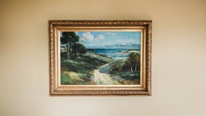 A framed landscape painting on a wall above a striped sofa. - Historic Downtown Manistee Apartment (Manistee)