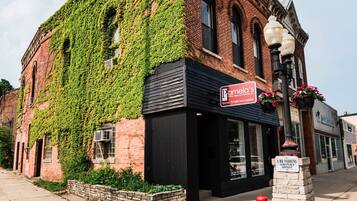 A brick building with ivy covering its exterior, a black awning, and a red fire hydrant in front.