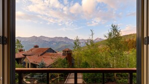 Une vue depuis un balcon doté d’une rambarde en métal, donnant sur une route avec une chaîne de montagnes en arrière-plan.