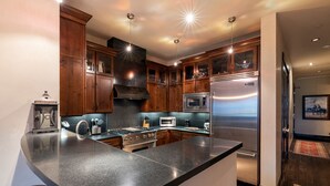 Une cuisine moderne dotée de plans de travail en granit, d’appareils électroménagers en acier inoxydable et d’armoires en bois.