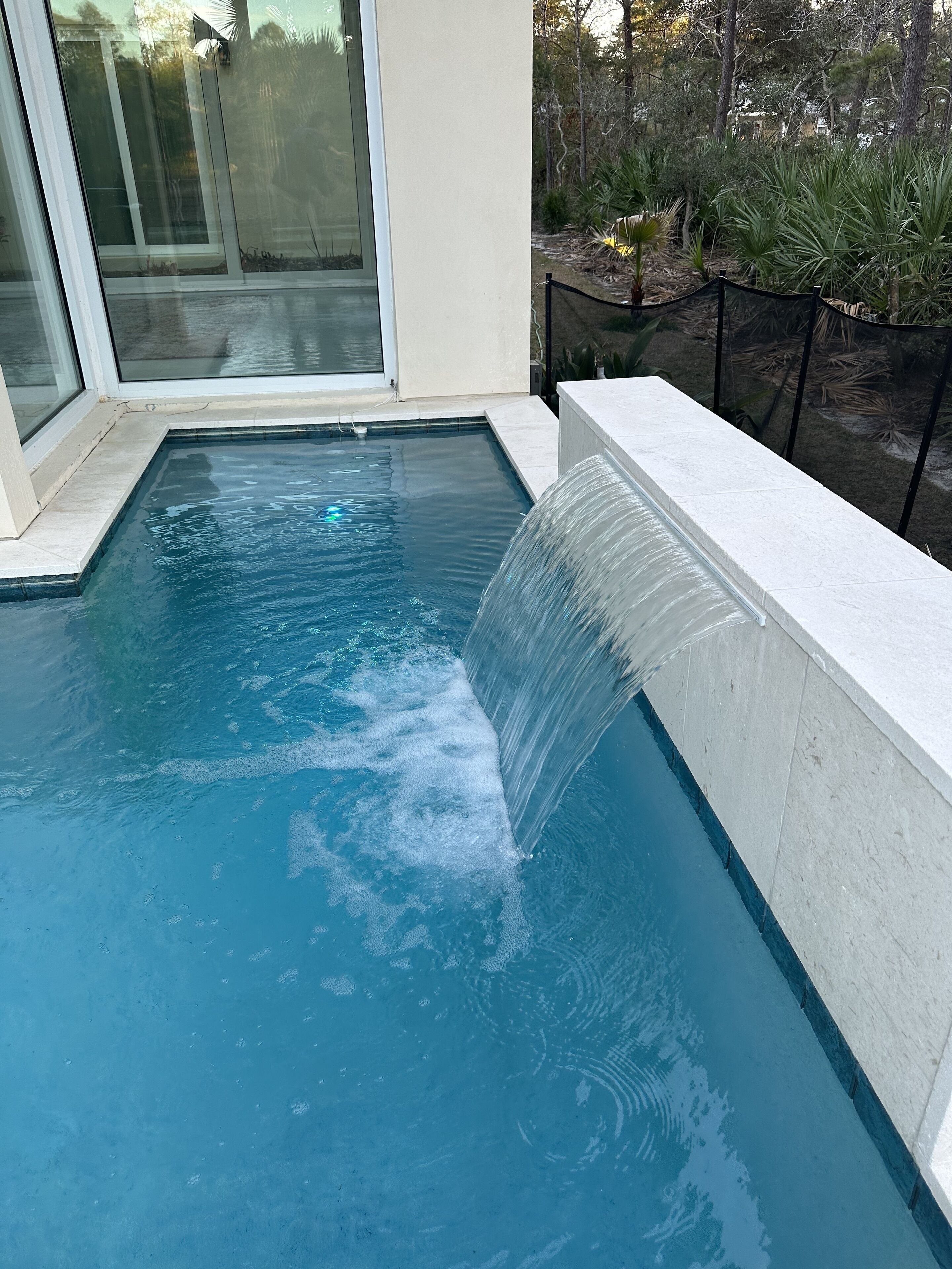 Ein Pool mit Wasserfall, umgeben von einem angelegten Garten und einem Glastür-Eingang.