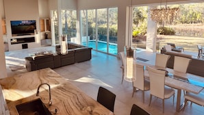 A modern living room with a large TV, a pool, and a dining area with outdoor seating. - Luxury, privacy and serenity close to beach, private pool (Santa Rosa Beach)