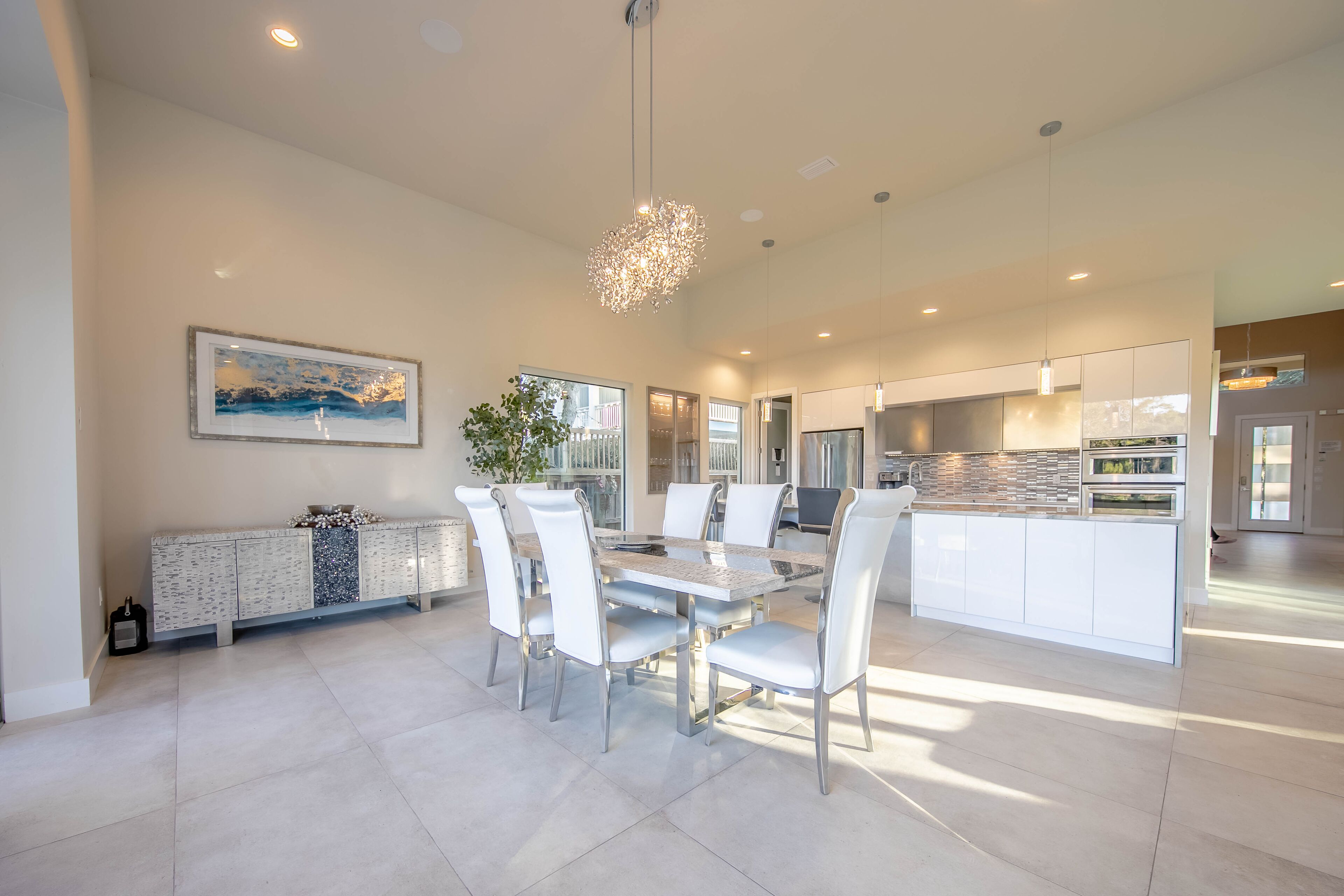 A spacious dining area with a round table, white chairs, and a modern chandelier.