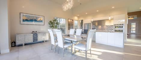 A spacious dining area with a round table, white chairs, and a modern chandelier.
