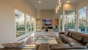 A spacious living room with a large window, a leather sofa, a glass coffee table, and a flat-screen TV. - Luxury, privacy and serenity close to beach, private pool (Santa Rosa Beach)