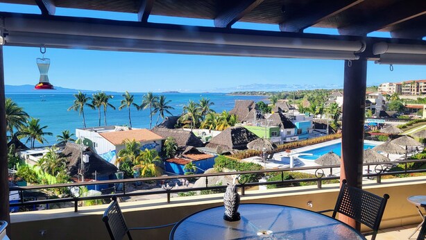 Un balcon avec vue sur une plage, des palmiers et une piscine.