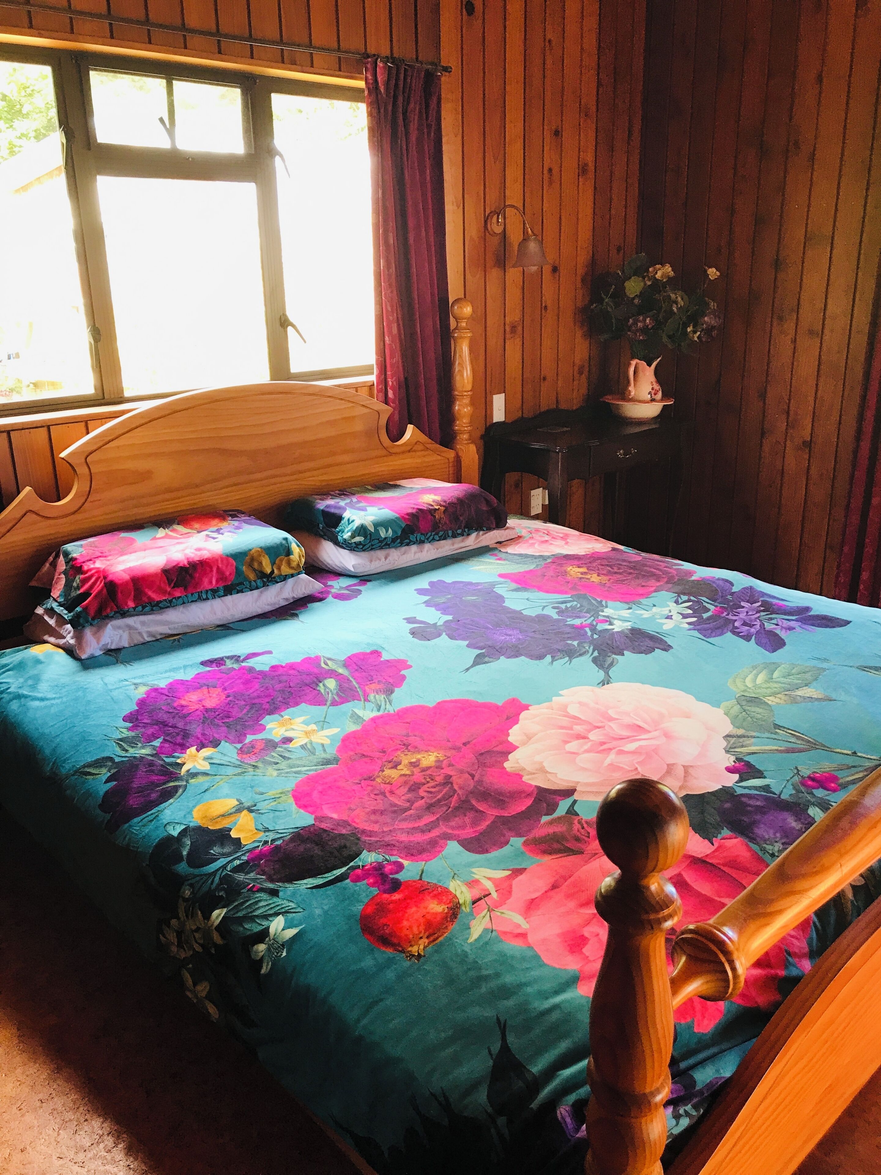 Een houten bed met een bloemenbedekking, een houten hoofdbord en een raam met gordijnen.