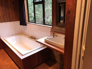 Un baño con dos lavamanos, una bañera, paneles de madera y una ventana con vista a árboles.