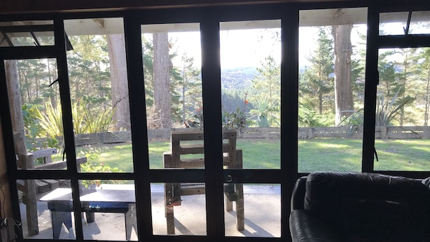 A room with large windows, a wooden bench, a small table, and a leather couch. - Large, genuine, Log House. 857 Church Rd. Kaitaia (Kaitaia)