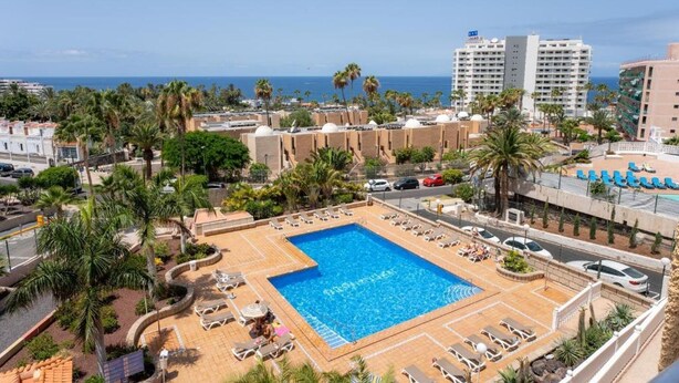 A resort with a large pool, palm trees, and a view of the ocean.