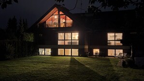 A modern two-story house with large windows and a balcony, surrounded by a well-maintained lawn.