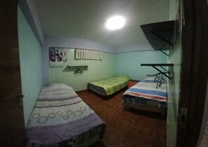 A small, dimly lit room with two single beds, a wall-mounted shelf, and a ceiling light.