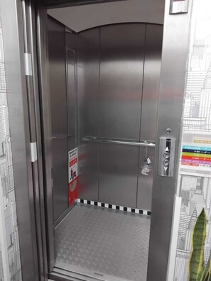 A metallic elevator interior with a glass door, a metal floor, and a door handle.