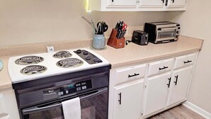 Una cocina con estufa, horno y tostadora. Hay armarios y una encimera.