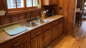 A kitchen with wooden cabinets, a double sink, and a window with frosted glass. - Sage Lake Huron Cottage  (East Tawas)