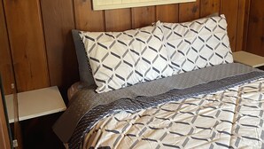 A wooden-paneled bedroom with a bed featuring a geometric patterned bedspread and pillows. A sign above the bed reads "RELAX BEACH". - Sage Lake Huron Cottage  (East Tawas)