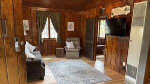 A cozy cabin interior with wooden walls, a sofa, a chair, a rug, and a television. - Sage Lake Huron Cottage  (East Tawas)