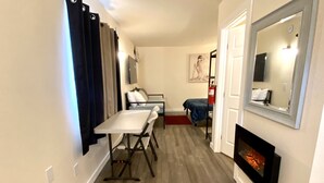 A compact room with a bed, a small table, a chair, a fireplace, and a mirror on the wall. - The Sever: Studio Guest Suite (Lynnwood)