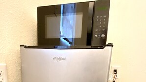 A Whirlpool refrigerator with a microwave on top, a power cord plugged in, and a wall socket on the left. - The Sever: Studio Guest Suite (Lynnwood)