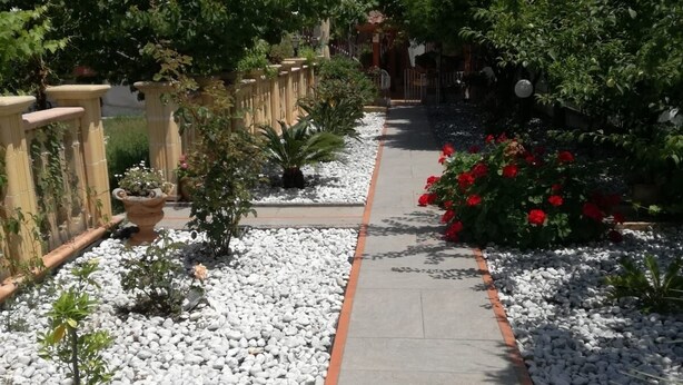 A pathway lined with white pebbles and red flowers, leading to a building with a tiled roof and a satellite dish. - House (Agropoli)