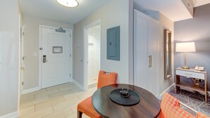 Habitación de hotel con una mesa de comedor, sillas, lámpara y una puerta.